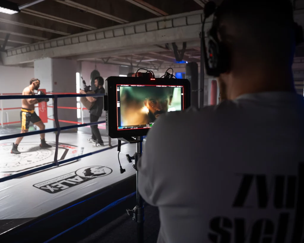 BTS z natáčania reklamného spotu Gam's. Detail na režisérsky monitor, v pozadí kameraman s ARRI Alexa a MMA bojovník Ivan Buchinger v ringu.